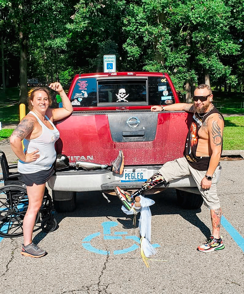 Portait of Team Amplife® Ambassadors Kara Wolter and Jason Loftiss wearing their prosthetics rested on a truck bed with the license plate, "PEGLEG"