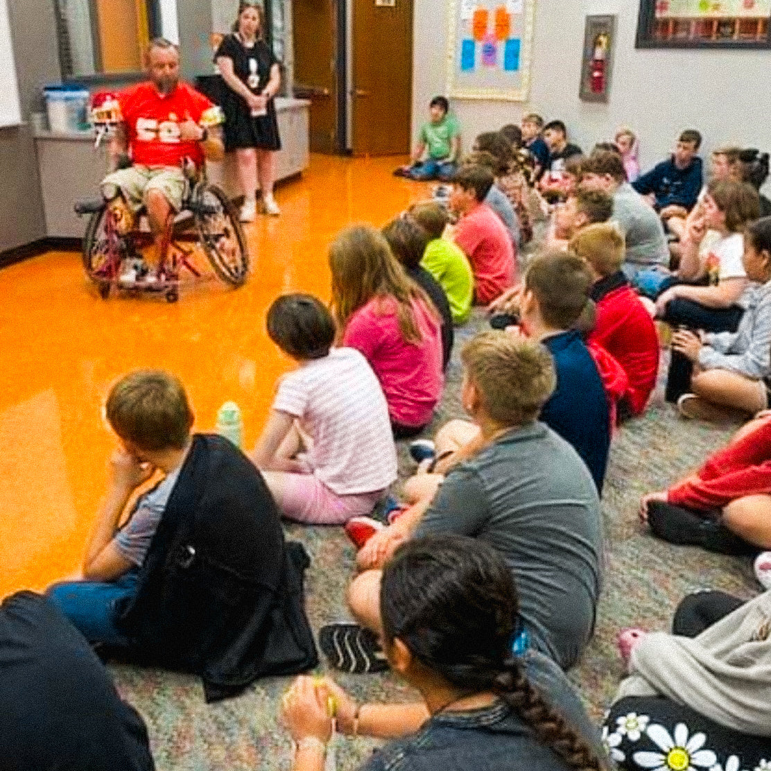 Team Amplife® Ambassador Jason Loftiss showing his wheelchair football gear to a group of students