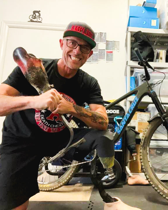 Portrait of Team Amplife® Ambassador Andrew May holding his prosthetic leg next to his mountain bike
